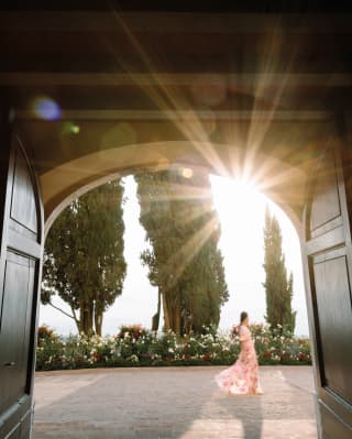 View through an arched doorway of a lady in floral dress walking by cypress trees