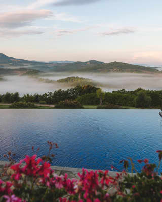 Looking over the hilltop pool to views of the rolling Tuscan countryside beyond as morning mist pools in the green valleys.