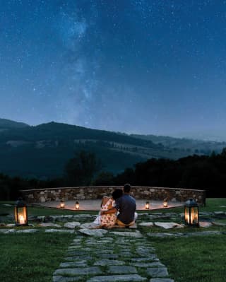 Stars sparkling in an inky-blue night sky over rolling Tuscan hills