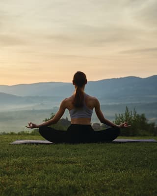 Lady in a lotus yoga pose on a lawn with views of sunrise over the Tuscan hills