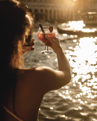Una donna che brinda con un cocktail mentre il sole tramonta su Venezia