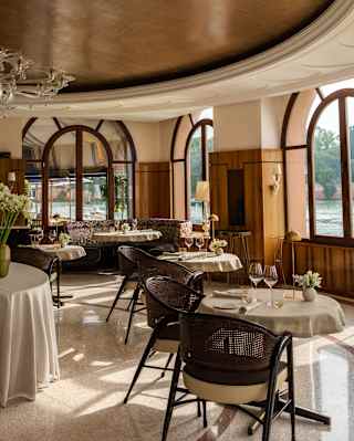View along a row of round dining tables laid for lunch in Oro, absorbing light and views from arched windows on to the canal.