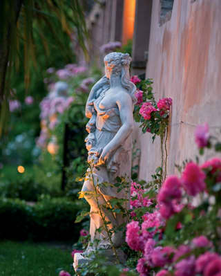 Close-up of a Venus statuette surrounded by pink flowers in a lamplit garden