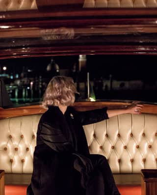 Blonde lady gazing out the back of a wood-panelled Venetian water taxi