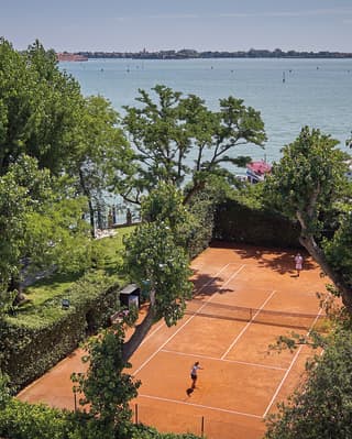 Aerial view of a clay tennis court surrounded by lush garden foliage