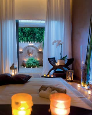 Candlelit spa treatment room with open patio doors leading to a courtyard beyond