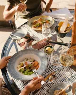 Guests enjoy a fresh light lunch with white wine, seen from above, close-up, at a sunny al fresco table at Curiña Restaurant.
