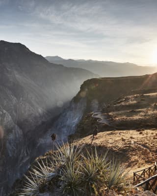 Sun bursting over the top of a shaded canyon under blue skies