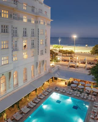 Glamorous lamplit outdoor pool in evening light next to a white hotel facade