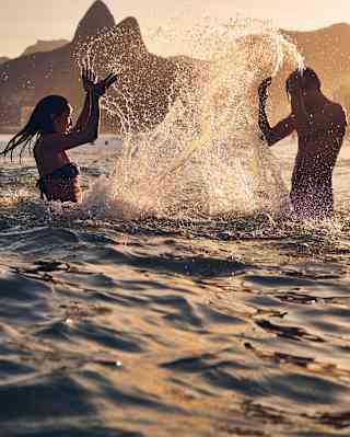 A man and a woman in the sea playfully splashing each other at sunset