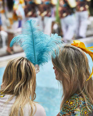 Two ladies wearing brightly coloured feather caps by a poolside