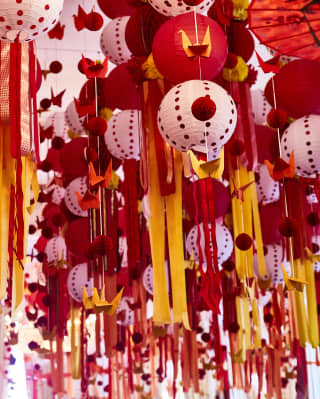 Paper lanterns, origami cranes and baubles hang with streamers of yellow and red in a forest of party ceiling decoration