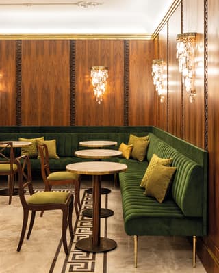 Green velvet banquette seating with circular marble-topped tables in a theatre bar