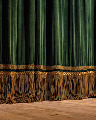 Close-up of a golden fringe detail on an emerald green stage curtain