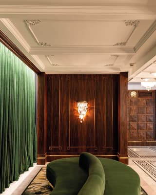 An s-shaped velvet bench with central backrest bolster snakes towards a wood panelled wall in an elegant theatre foyer