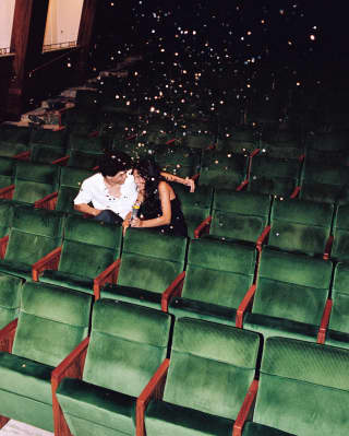 With confetti in the air, a man in a white shirt and a woman in black cosy up in the green velvet seats of the empty theatre.