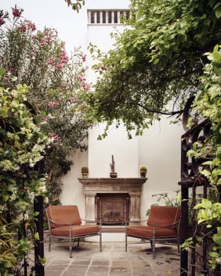 Two lounge chairs in a garden courtyard either side of a stone fireplace