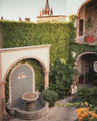 View over Casa Limón's courtyard with fountain alcove and ivy-clad walls, and the spires of Parroquial de San Miguel behind.