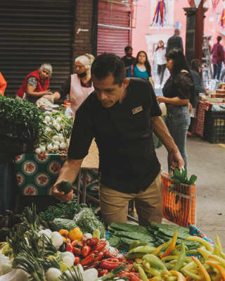 Chef Rubén Yañez tests the ripeness of an avocado at a vibrant food stall during a market tour with his Sazón cooking class.