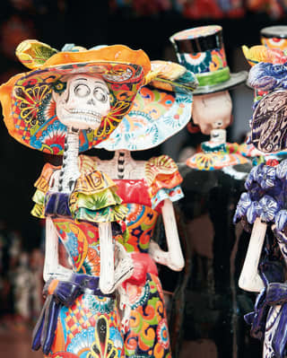 Rows of vibrantly-coloured ceramic 'day of the dead' figurines in patterned dresses and hats