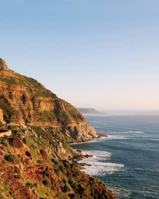 Ocean road curving around a sloping cliff beside a calm ocean at sunset