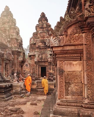 Two orange-robed monks among an ornate Khmer temple complex