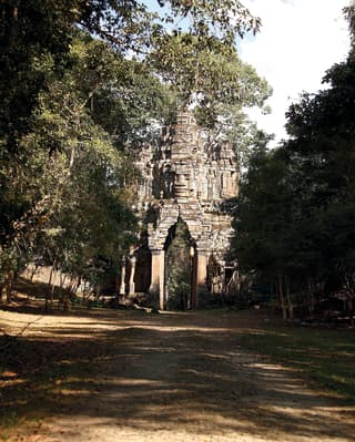 Vast stone temple gate carved with a god-like figure and lined with trees