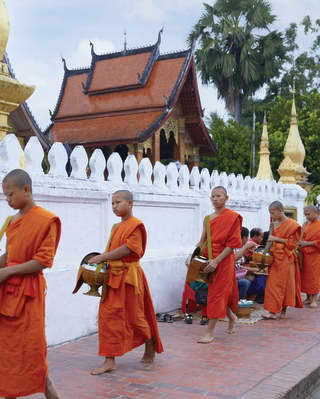 Five orange-robed monks in a Tak Bat procession outside a temple