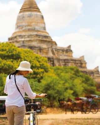 Lady wheeling a bicycle towards an ancient pagoda