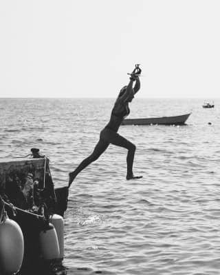 A black and white photo of a woman jumping into the sea