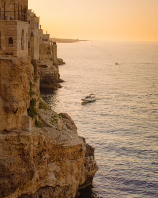 In golden sunset light, a boat heads for an unseen cove tucked between headlands and their cliff houses on Taormina's coast.