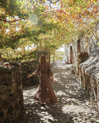Lady in a summer dress walking along a cobbled path under the shade of trees
