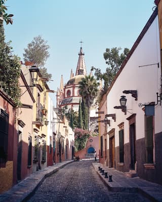 Pastellfarbene Häuser an einer schmalen gepflasterten Straße, die zu einer Kirche führt