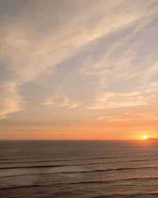 Looking out at the Pacific sea as it scrolls back towards Lima, its horizon smudged apricot orange by a golden setting sun.