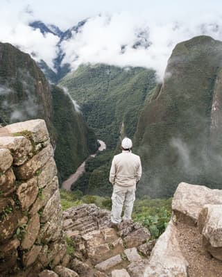 A man seen from behind as he looks down at the Urubamba River weaving through the colossal foothills of the Sacred Valley.