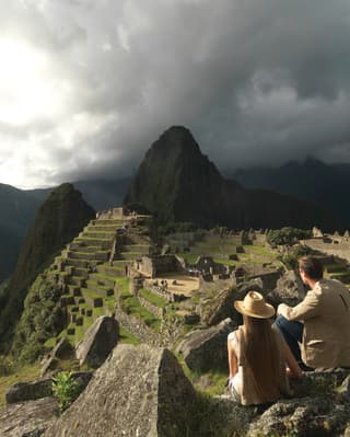 Casal sentado em uma rocha com vista para a cidadela Inca de Machu Picchu