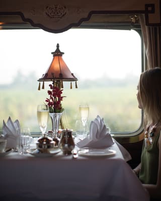 Lady at a table with two champagne glasses gazing out a train window