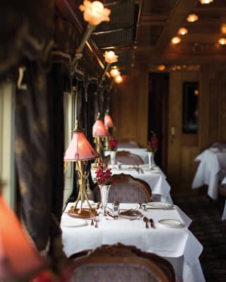 Rows of formal dining tables lining a luxurious train restaurant carriage