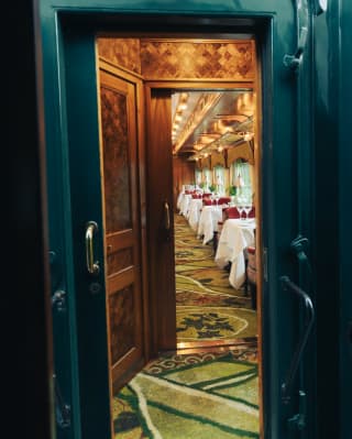 Doorway view of the Malaya dining car, exotic and elegant with jade pattered carpet, red chairs and white-clothed tables.