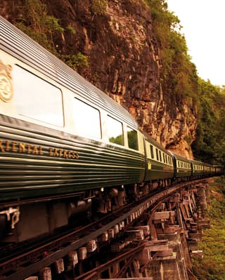 Vagones de tren de color crema y verde recorriendo un puente ferroviario de madera