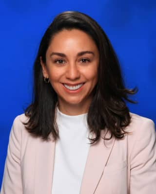 Area Sales Director, Erika Toto, smiles to camera with shoulder-length black hair, wearing a pale pink suit over a white top.