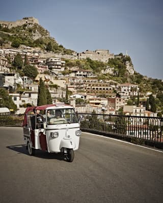 A classic white Piaggeo Ape offers guests great views beyond its open red cabriolet roof, as it explores Taormina's streets