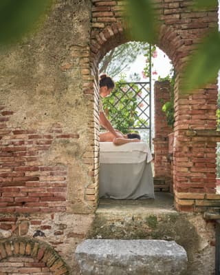 View through an arch in a brick wall of a spa therapist massaging a lady