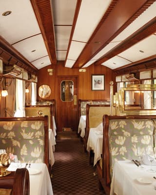 Looking along the dining carriage with upholstered sage fabric seating, maroon patterned carpet and glossy wood panelling.