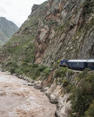Royal blue train carriages snaking alongside a mountain and rushing river