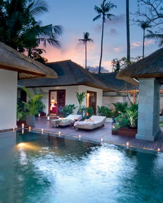 Balinese villas around a freshwater infinity pool surrounded by candles at sunset