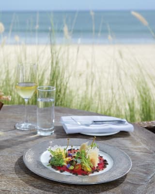 Close-up of a salad dish on a table beside a sandy beach