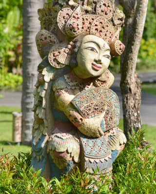 At the Surya Temple, a Hindu statue with an ornate headdress, holding a fan, sits in the Pura - an open-air prayer space.
