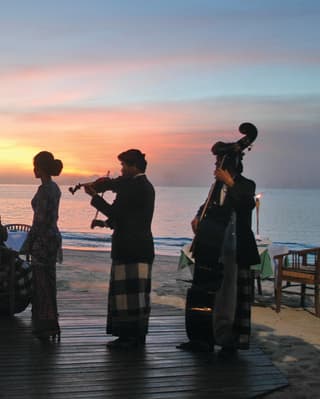Six musicians, with cello, double base and violin, are silhouetted against the sunset sky and sea during a beach concert.