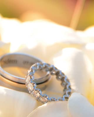 Two white-gold wedding bands - one plain and the other banded with diamonds - rest on a cushion of frangipani flowers.